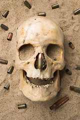 Image showing skull lying in the sand, scattered rifle and pistol cartridges. concept of war