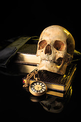 Image showing human skull on a book next to the clock. concept of black magic