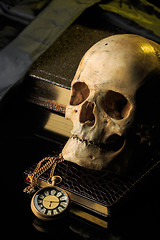 Image showing human skull on a book next to the clock. concept of black magic