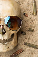 Image showing skull lying in the sand, scattered rifle and pistol cartridges. concept of war