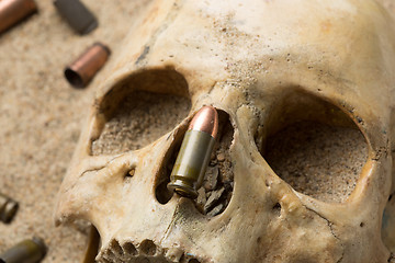 Image showing skull lying in the sand, scattered rifle and pistol cartridges. concept of war
