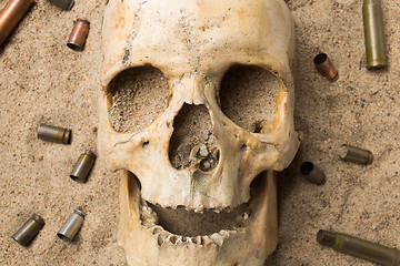 Image showing skull lying in the sand, scattered rifle and pistol cartridges. concept of war