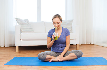 Image showing happy woman with smoothie sitting on mat at home