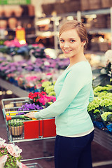 Image showing happy woman with shopping trollye buying flowers