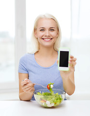 Image showing smiling woman with smartphone eating salad at home