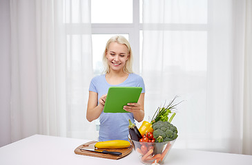 Image showing smiling young woman with tablet pc cooking at home