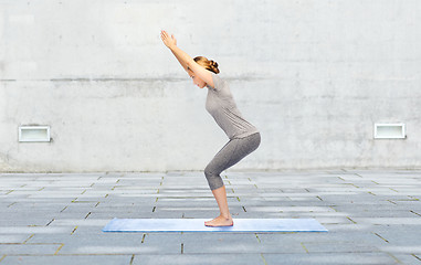 Image showing woman making yoga in chair pose on mat outdoors