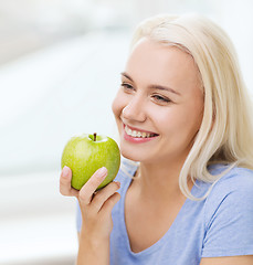 Image showing happy woman eating green apple at home