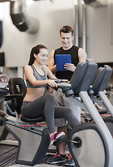 Image showing happy woman with trainer on exercise bike in gym