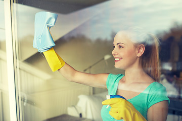 Image showing happy woman in gloves cleaning window with rag