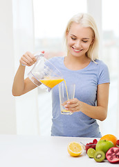 Image showing smiling woman pouring fruit juice to glass at home