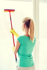 Image showing happy woman in gloves cleaning window with sponge