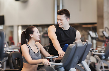 Image showing happy woman with trainer on exercise bike in gym