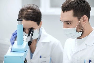 Image showing scientists in masks looking to microscope at lab