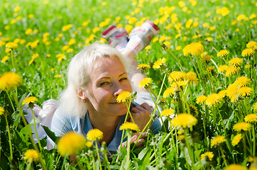 Image showing A woman lies in a clearing and sniffs a flower  