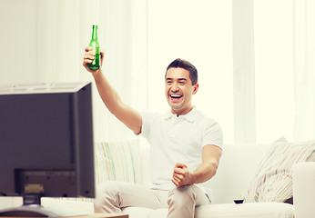 Image showing smiling man watching tv and drinking beer at home