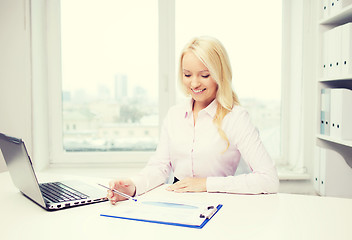 Image showing smiling businesswoman reading papers in office