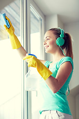 Image showing happy woman with headphones cleaning window