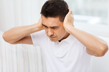 Image showing unhappy man closing his ears by hands at home