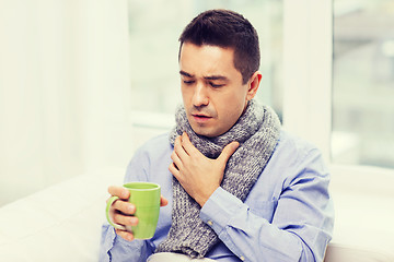 Image showing ill man with flu drinking tea and coughing at home