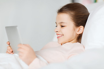 Image showing happy girl lying in bed with tablet pc at home