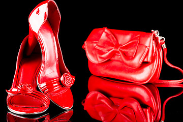 Image showing luxury red high heel women shoes and a bag on black background. reflection