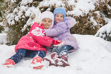 Image showing Two girls are sitting in a snowdrift snow and hugging each other