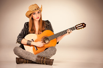 Image showing The beautiful girl in a cowboy\'s hat and acoustic guitar.