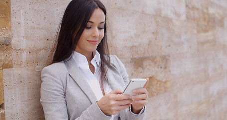 Image showing Female worker texting and leaning against wall