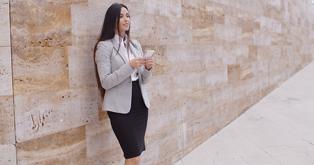 Image showing Female worker texting and leaning against wall