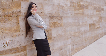 Image showing Happy woman talking on phone and leaning on wall