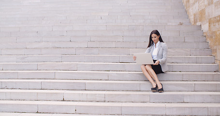 Image showing Pretty young worker sitting on steps with laptop