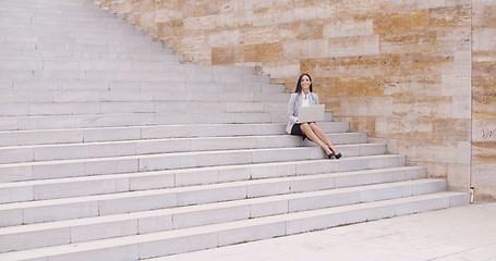 Image showing Pretty young worker sitting on steps with laptop