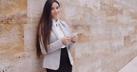 Image showing Business woman leaning against wall texting