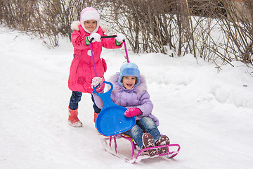 Image showing The older girl rolls the younger girl on a sled in the yard