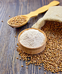 Image showing Flour buckwheat in bowl and spoon with cereals on dark board