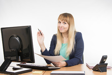 Image showing Business woman holding a sheet of paper and a pen and working on the computer in the office