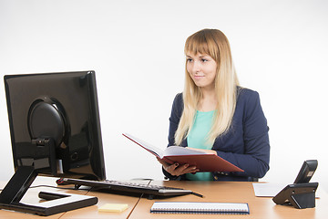 Image showing Happy business woman holding a book in the hands of the office and looking at the computer