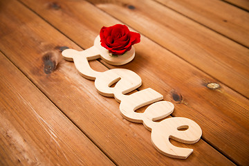 Image showing close up of word love cutout with red rose on wood