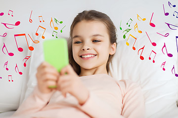 Image showing happy girl lying in bed with smartphone over notes