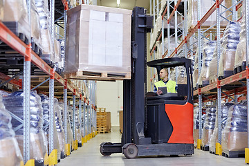 Image showing man with tablet pc operating forklift at warehouse