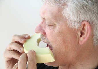 Image showing Older man eating melon slice  