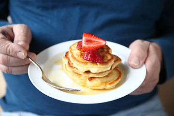 Image showing Man with plate of strawberry-topped pancakes  