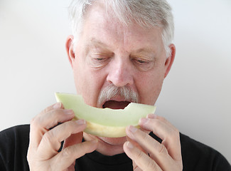 Image showing Older man eating melon slice 