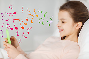 Image showing happy girl lying in bed with smartphone over notes