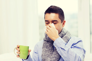 Image showing ill man with flu drinking tea and blowing nose