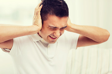 Image showing unhappy man closing his ears by hands at home
