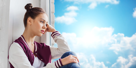 Image showing sad pretty teenage girl sitting on windowsill