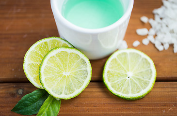 Image showing close up of body lotion in cup and limes on wood