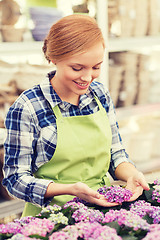 Image showing happy woman taking care of flowers in greenhouse